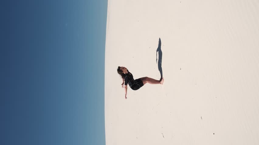 Fitness yoga woman stretching on the sand. Fit sportswoman doing yoga. Side view of the whole body of a slim young woman in a black top. Sport and healthy lifestyle concept
