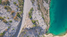 AERIAL TOP DOWN Autumn coloured shrubs, road and rocky landscape by the blue sea. Winding Adriatic highway leading through picturesque coastline with vegetation coloring in vivid shades of fall season