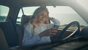 Girl looking social media in telephone sitting retro car at beautiful sunny ocean coast close up. Happy carefree woman at steering wheel messaging on modern smartphone. Smiling blonde watching phone. - Powered by Shutterstock - Get 15% off with code: PIKWIZARD15