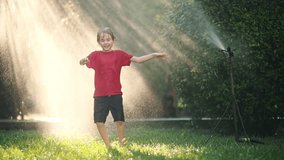 Slow motion video of funny little boy playing with garden sprinkler in sunny backyard.Elementary school child laughing, jumping and having fun with spray of water.Summer outdoors activity for children