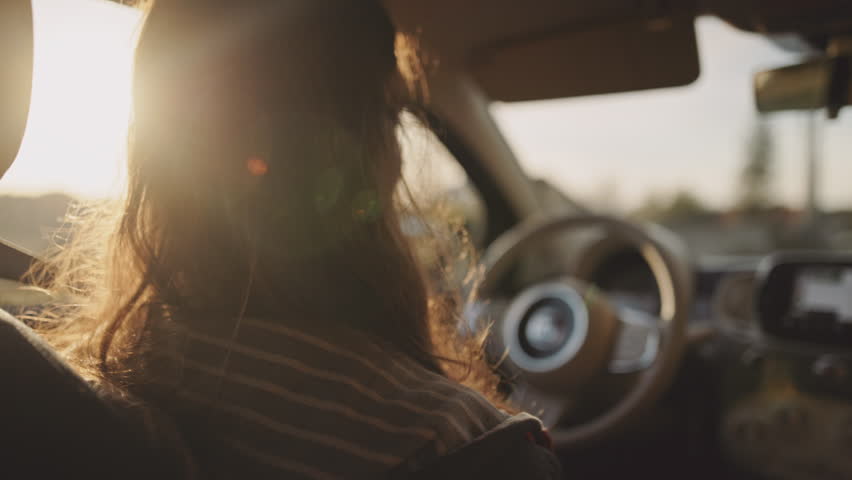 Man driving a car at sunset. Unrecognizable male driver holding steering wheel, sunrise, morning or evening road with lens flare. Young gen z man traveling in a vehicle, road trip.