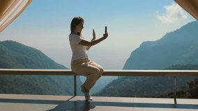 Travel blogger records video selfie or greetings for blog on mobile phone with beautiful mountain view in background. Life and work of influencers, travel, outdoor lifestyle, camping and vacation