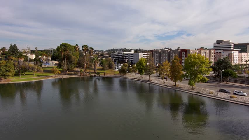backwards aerial footage of a gorgeous autumn landscape with a lake, a water fountain, lush green trees and cars driving along the street at Lincoln park in Los Angeles California USA