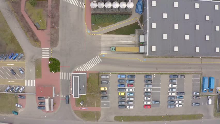 Trucks with semi-trailers stand on the parking lot of the logistics park with loading hub and wait for load and unload goods at warehouse ramps at sunset. Aerial view