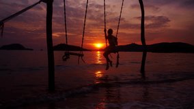 A video of a girl playing on a swing near the shore at a beach in Thailand during sunset