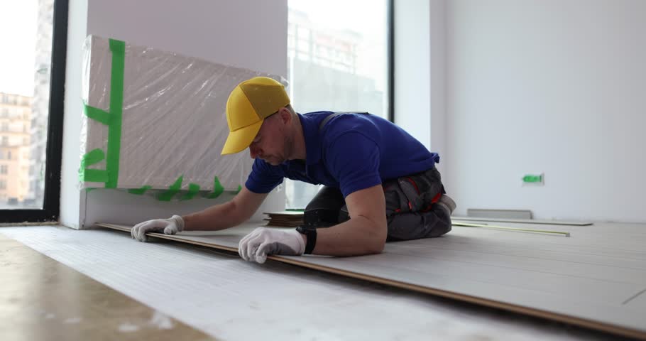 Worker with cap installs laminate board on floor in office