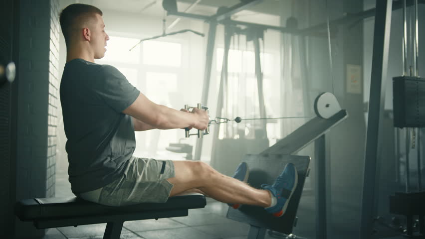 Profile shot of fit man performing seated cable row on cable crossover machine. Sportsman sits on the bench pulling the handle toward lower abdomen. High quality 4k footage
