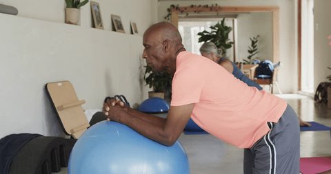 Diverse seniors using exercise balls in pilates class with female coach, unaltered, in slow motion. Exercise, retirement and healthy senior lifestyle. Video Stok