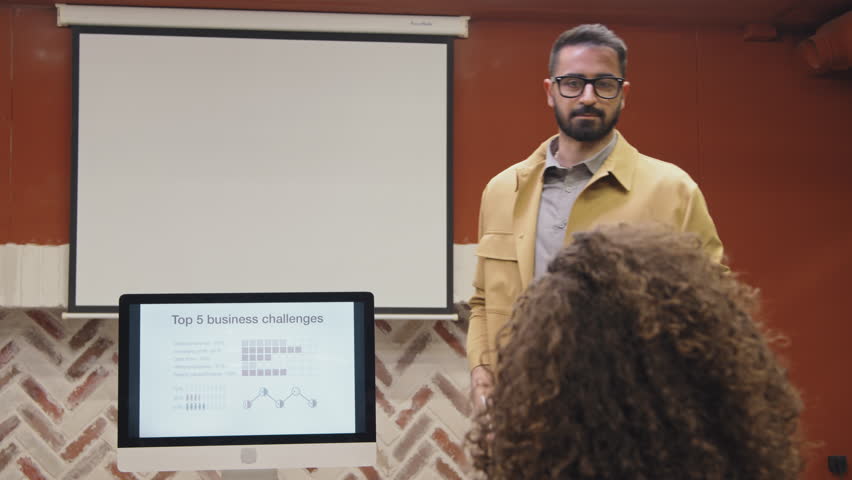 Medium shot of casually dressed confident Arab male career coach conducting business training for corporate employees in conference room of coworking facility, laughing and talking to diverse audience