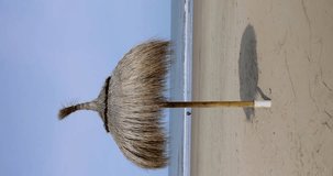 An umbrella made of straw on a sandy beach on the sea. Vertical video.