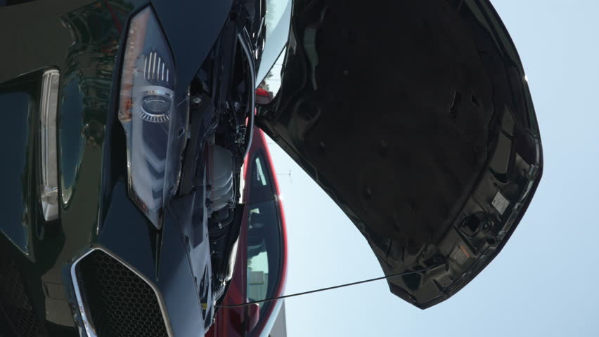 American muscle car stands with its hood up in open air parking lot. People are reflected in clean polished body, clean engine is demonstrated to passers by at meeting of automobile club.