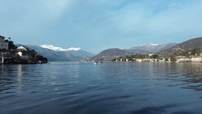 Drone flying at low altitude over waters of Orta lake with boats sailing on sunny day, Italy. Aerial view and sky for copy space