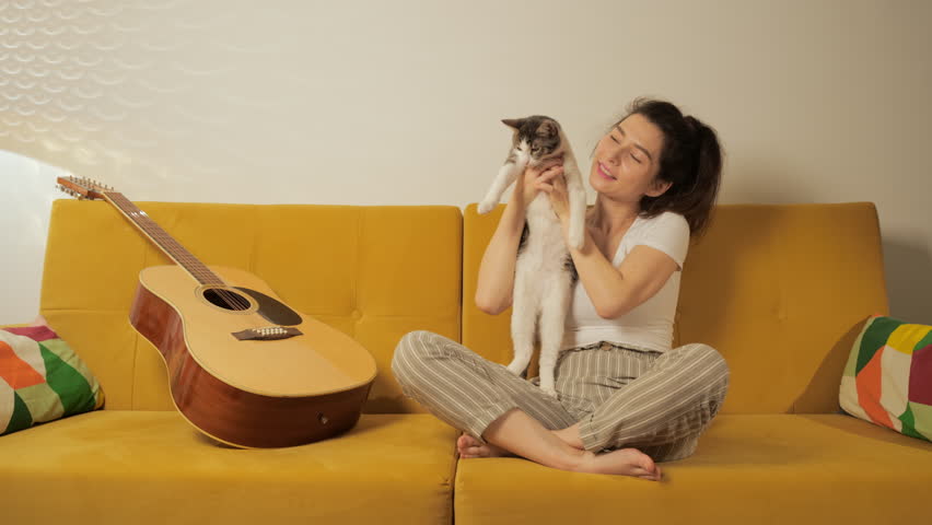 Adorable domestic animal concept. Young beautiful Asian woman relaxing and playing with her lovely cat on coach in living room at night. Girl and her little funny kitty together. Royalty-Free Stock Footage #1103957971