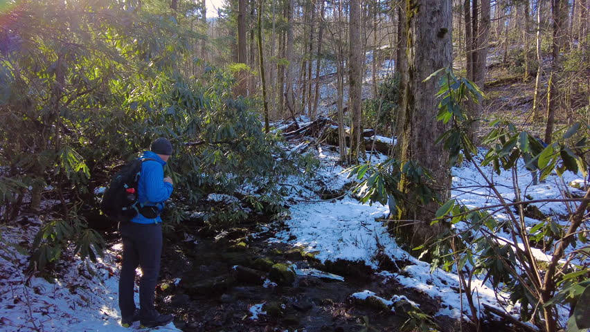 Man Hikes Across Creek in Snowy Forest in the Smokies