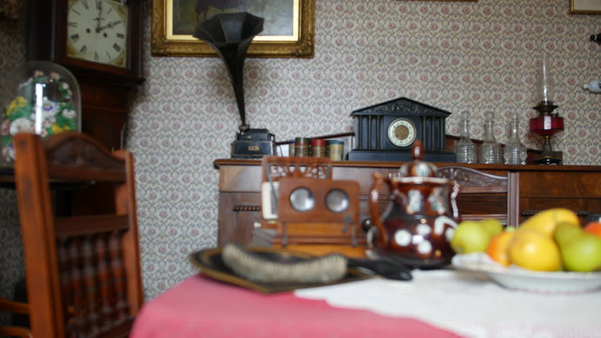 A victorian living room with dining table and phonograph with a grandfather clock and gaslight