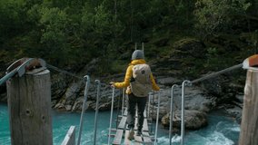 Woman in hiking outfit, yellow jacket and backpack walk over epic suspension bridge in national park. Cinematic wanderlust adventure in wilderness. Woman walk over mountain river in Scandinavia - Powered by Shutterstock - Get 15% off with code: PIKWIZARD15