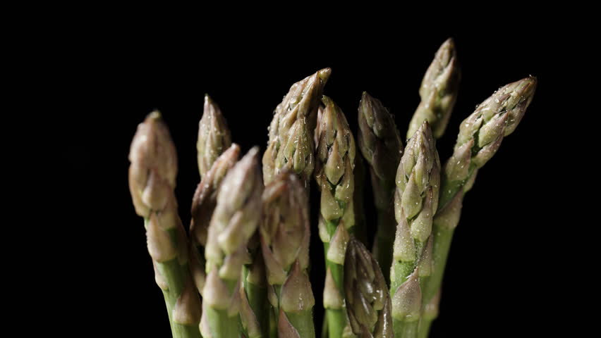 A bundle of asparagus spears slowly rotates on a black background, captured in a close-up, providing a detailed view of their textures and shapes.