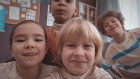 Handheld POV of group of multicultural first grade kids recording video of themselves having fun in classroom