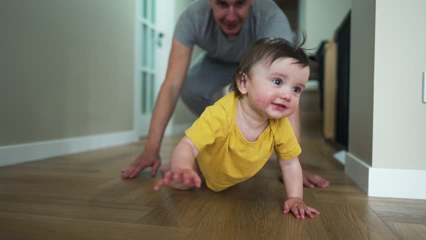Happy family.Baby crawls on floor with his father.Girl smiles and crawls on floor of house.Dad plays with his daughter at home.Home kindergarten.Father day in kindergarten.Happy baby crawling on floor Royalty-Free Stock Footage #1103981819