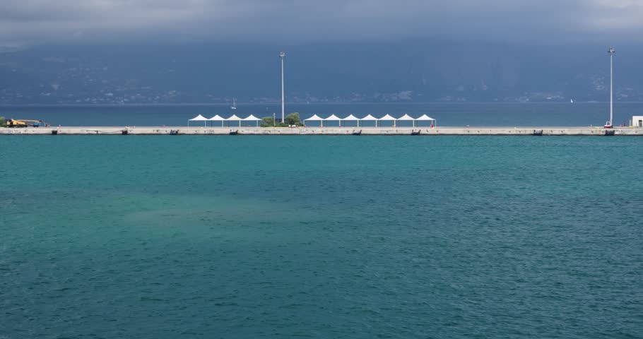 Beautiful view of pier with sun umbrellas near sea at port of Corfu island, Greece
