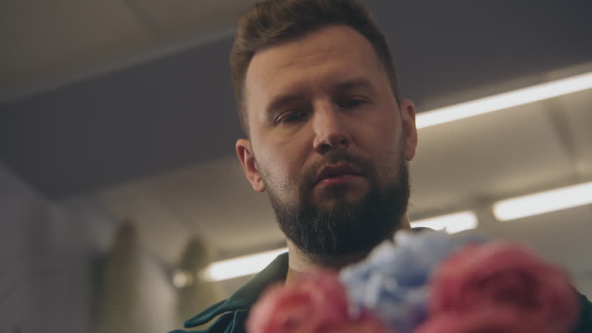 Close up shot of florist entrepreneur working in flower shop. Concentrated man collects beautiful bouquet uses fresh flowers to sale or delivery. Retail floral business and entrepreneurship concept.