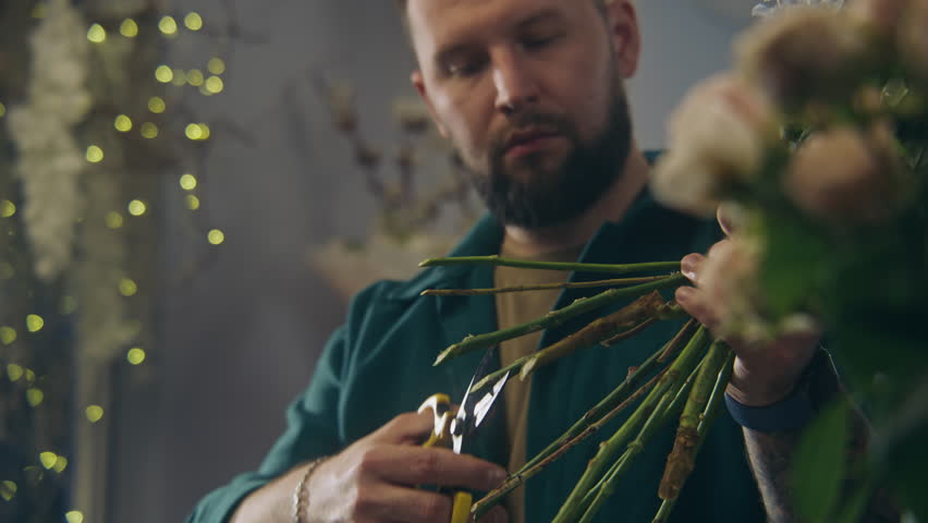 Close up shot of professional florist cutting stems of fresh flowers using secateurs and looking at arrangement. Man creates beautiful bouquet to sale. Retail business and entrepreneurship concept.