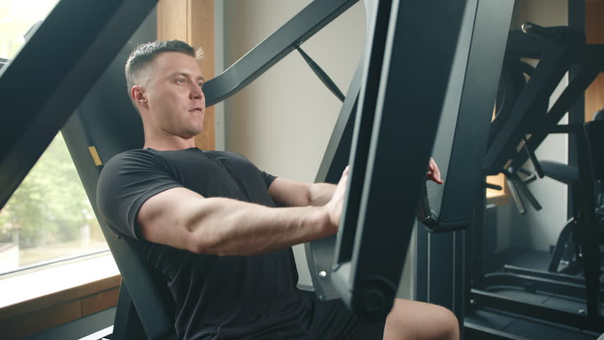 Middle-aged athlete performs exercises on chest press machine. Chest workout. Sportsman holds handles, pushes outwards and fully extends arms. High quality 4k footage Royalty-Free Stock Footage #1103991077