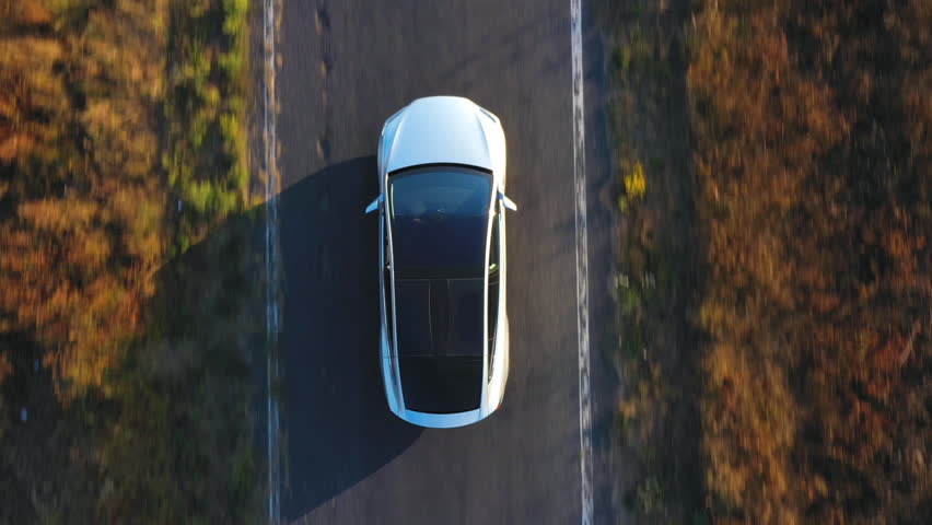 Aerial shot of electrical car driving on country road at summer evening. New SUV vehicle speeding through highway. Ecology friendly car riding on electric charge along motorway. Top view Close up