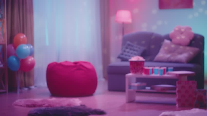 Defocused interior of a room decorated for a party. The room is decorated with balloons, popcorn, pizza and paper cups are on the table. The room is illuminated by the glare from the disco ball. Royalty-Free Stock Footage #1104004165