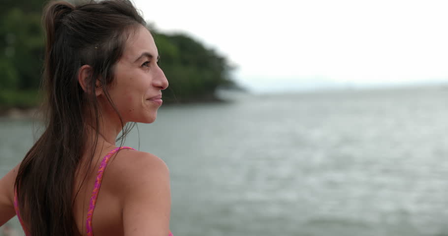 Woman stands on beach overlooking ocean in morning - from behind