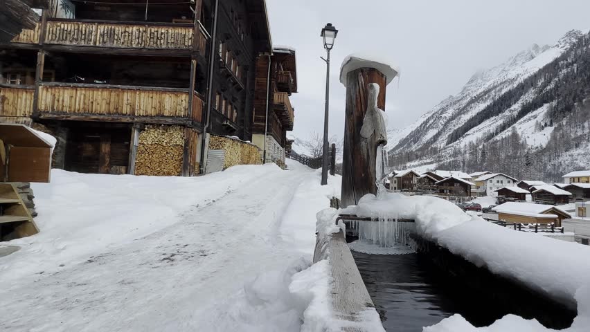 The small village of Blatten in the Lötschental valley in Switzerland. Snowy village in the Swiss mountains with lots of snow and ice. The fountain is frozen over