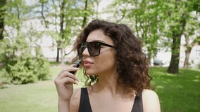 close portrait of a young woman who smokes an electronic cigarette in a city park 4k