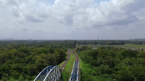 Aerial view of the train passes through the area of green trees and rice fields with cloudy sky during the day. The train runs away and disappeared from sight - 4K drone footage