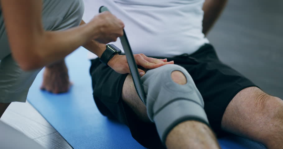 Physiotherapy, training and knee with a bandage after injury, accident or rehabilitation. Help, fitness and hands of a doctor with a brace for leg of a patient for muscle care, recovery and health Royalty-Free Stock Footage #1104010945