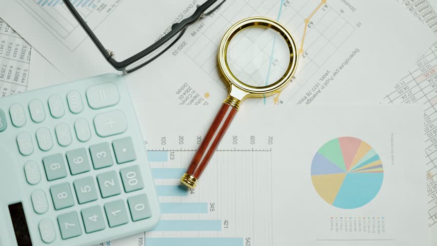 Documents with magnifying glass and calculator. Printed stock graphs and charts. Analyzing financial data report and business concept. Profit and tables on work desk - Powered by Shutterstock - Get 15% off with code: PIKWIZARD15