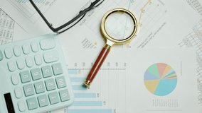 Documents with magnifying glass and calculator. Printed stock graphs and charts. Analyzing financial data report and business concept. Profit and tables on work desk - Powered by Shutterstock - Get 15% off with code: PIKWIZARD15