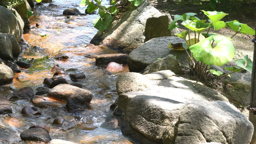 Small stream flowing over boulders in urban nature park.