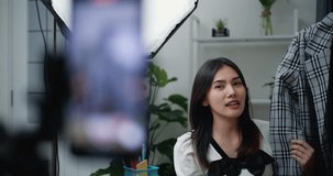 Footage slow motion shot of Young Beautiful Asian women live streaming to sale new fashion clothes at home studio, They enjoy to talking in front of smartphone, influencer on social media concept