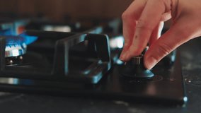Person using kitchen burner with hand. Ignited bright blue flame, fire for cooking. Background black color cooktop, hob. Gas stove being turned on by lit burner. Natural gas inflammation close up. - Powered by Shutterstock - Get 15% off with code: PIKWIZARD15