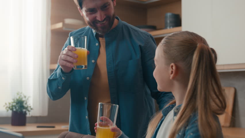 Caucasian father with little daughter child girl drinking fresh drink healthy tasty orange juice healthcare dad help using laptop teach browsing computer kid happy family dinner breakfast at kitchen Royalty-Free Stock Footage #1104020379