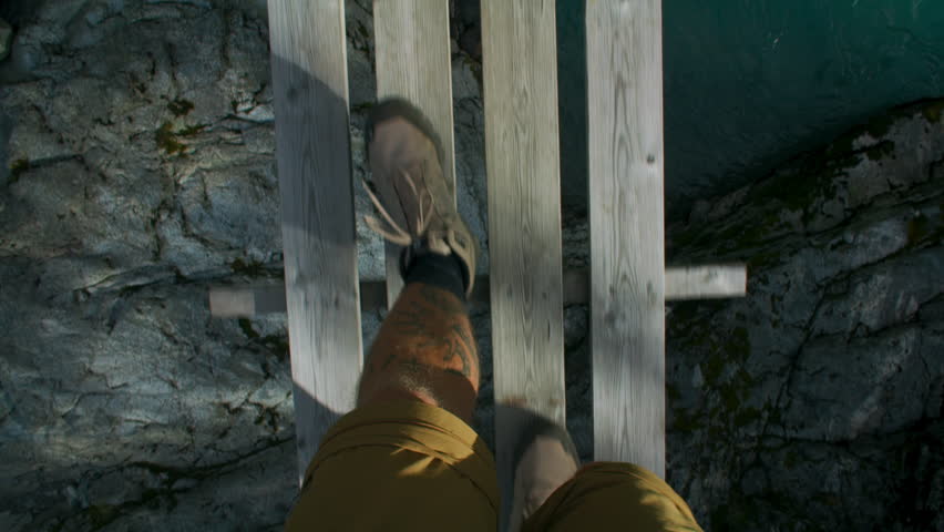 POV of man in hiking boots walk over flimsy wooden suspension bridge over wild mountain river. Epic hike adventure, or outdoor exploration concept. Shoes walk on wooden bridge Royalty-Free Stock Footage #1104021289