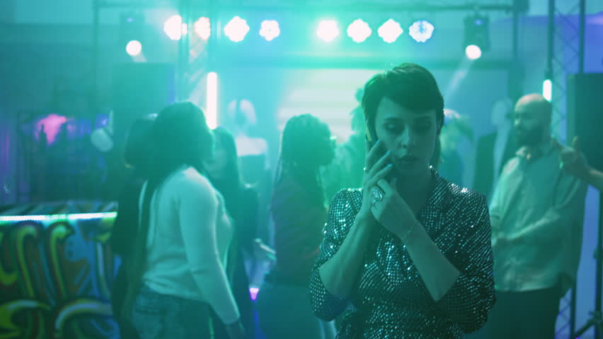 Young woman trying to talk on phone at discotheque, answering phone call on dance floor. Girl having conversation while the music is playing loud, social gathering event. Handheld shot. | Shutterstock HD Video #1104023427