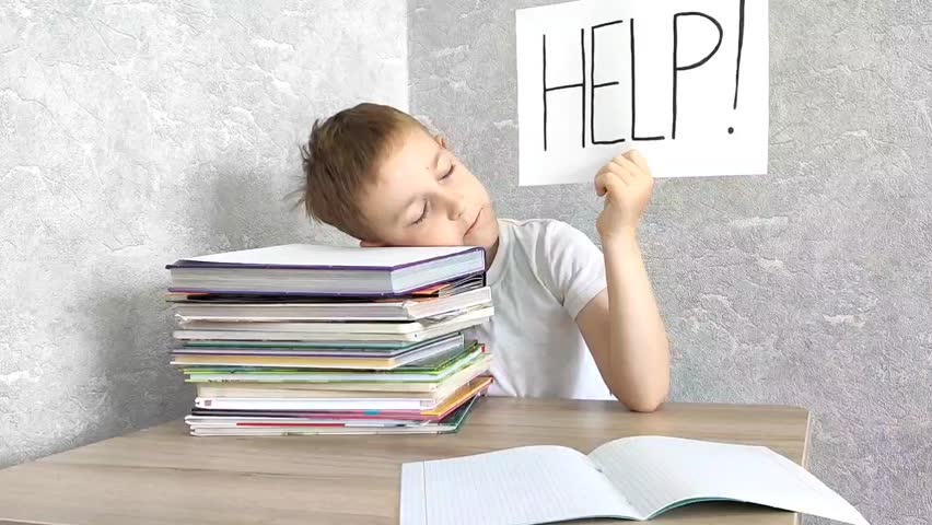 sad boy sits at a table with books and holds a paper with the word Help. Learning difficulties, ADHD, education concept. Royalty-Free Stock Footage #1104027897