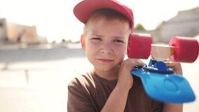child boy with skateboard. boy in a red cap with a skateboard on the playground portrait. skateboarder child close-up outdoors sun glare. lifestyle kid skateboarder looking at the camera