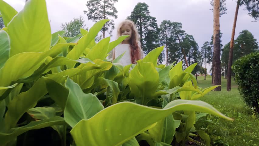 Tender little angel girl among green leaves. In her hands is a feather from a wing.