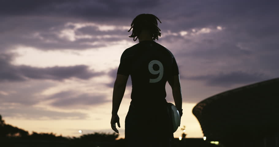 Back, sunset and a man on a field for rugby, sports and ready to start training. Night game, dark and closeup of an athlete player holding a ball for sport, competition and fitness at a stadium Royalty-Free Stock Footage #1104030625