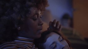 Close-up of young multiracial lesbian couple relaxing at home watching a movie at television. Women affectionate caress her partner hair as enjoy real domestic life night. Happy LGBT relationships - Powered by Shutterstock - Get 15% off with code: PIKWIZARD15