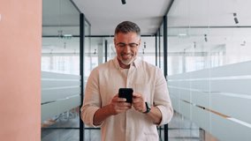 Mature Latin or Indian businessman walking with smartphone in office. Middle aged manager using cell phone mobile app. Digital technology application and solutions for business success development. - Powered by Shutterstock - Get 15% off with code: PIKWIZARD15