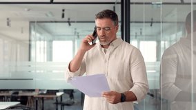 Middle aged Latin or Indian businessman walking, having call on smartphone with business partners and looking at documents. Mature Hispanic man talking by mobile cellphone at work in modern office.  - Powered by Shutterstock - Get 15% off with code: PIKWIZARD15