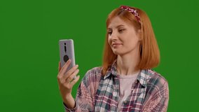 Woman having fun video chatting using mobile phone over green screen background. Female on video call having an interview. Technology concept.